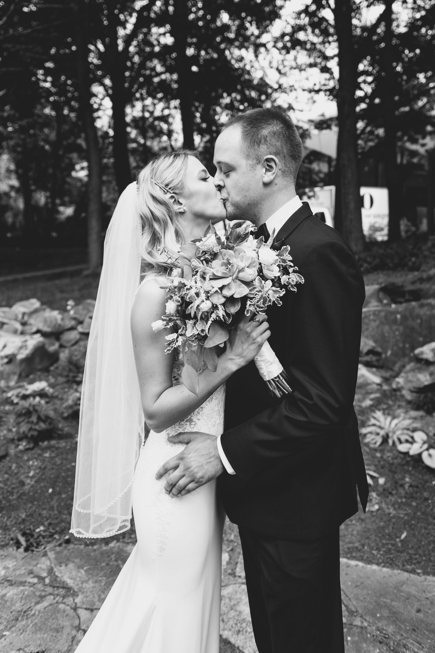 An intimate black and white wedding portrait showing a tender moment with a floral bouquet.