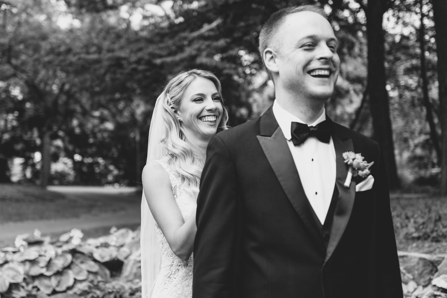Black and white photo of a couple joyfully laughing together outdoors in formal wedding attire.