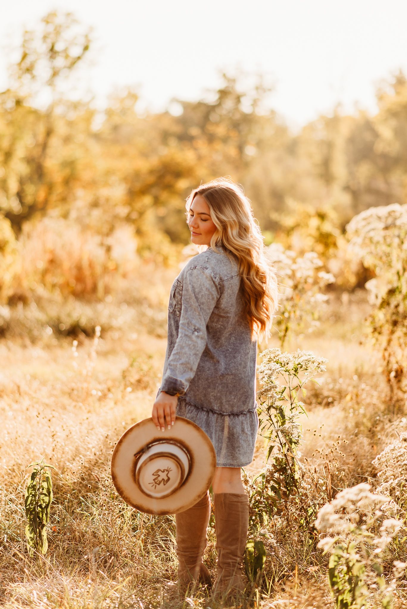 Fashion portrait in a golden field at sunset with cowboy boots and hat.