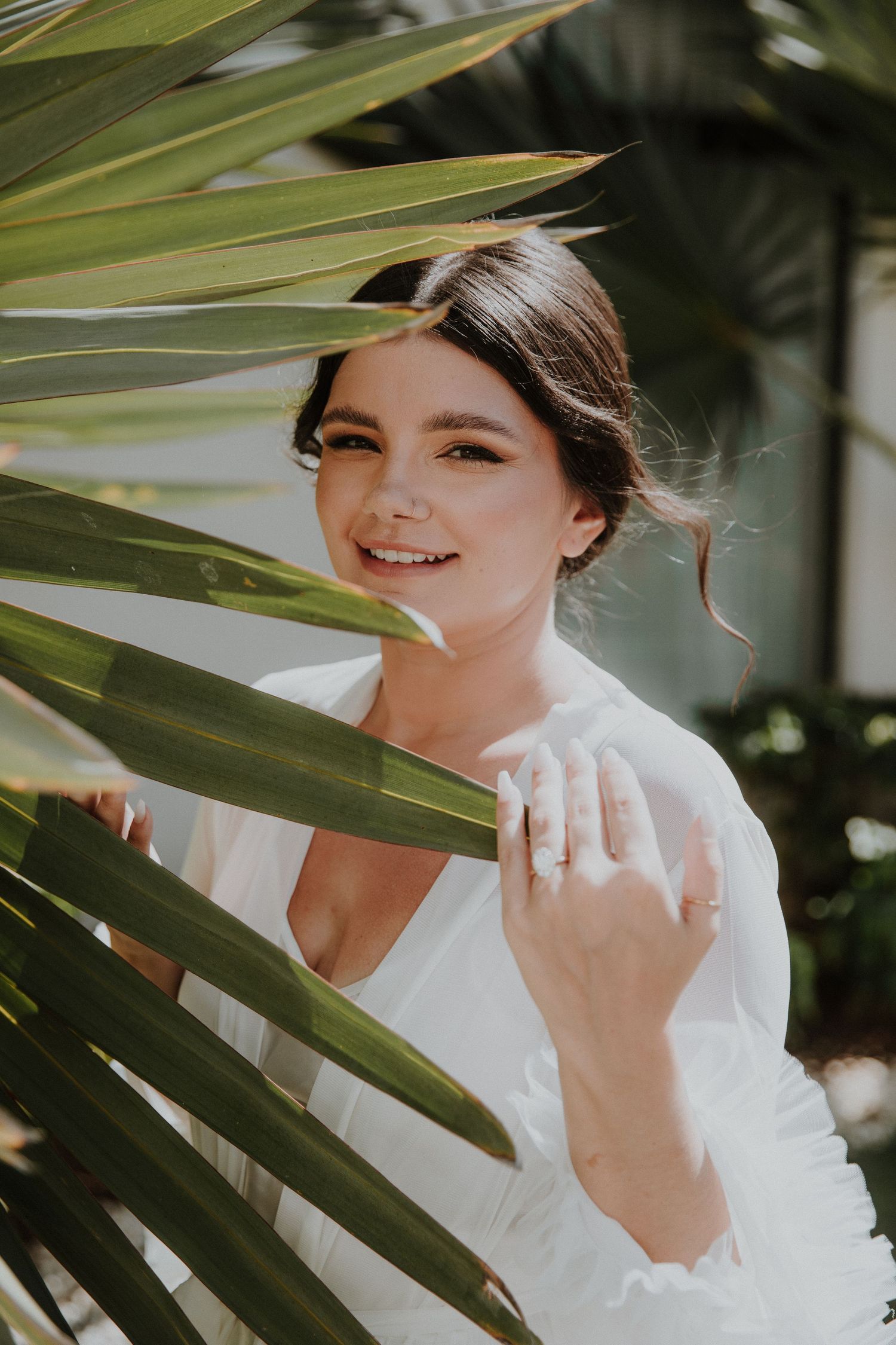 Bridal portrait through tropical palm leaves showing engagement ring.