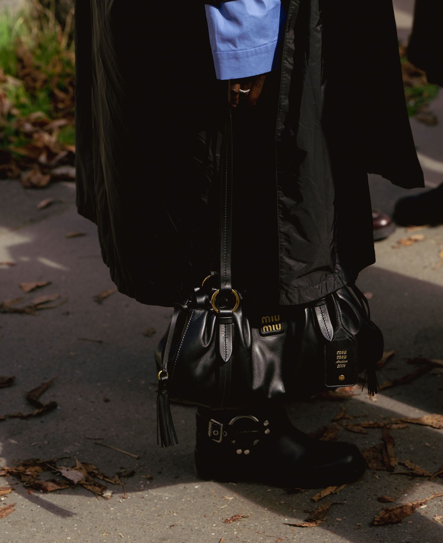 Black leather bucket bag and boots photographed against fallen leaves.