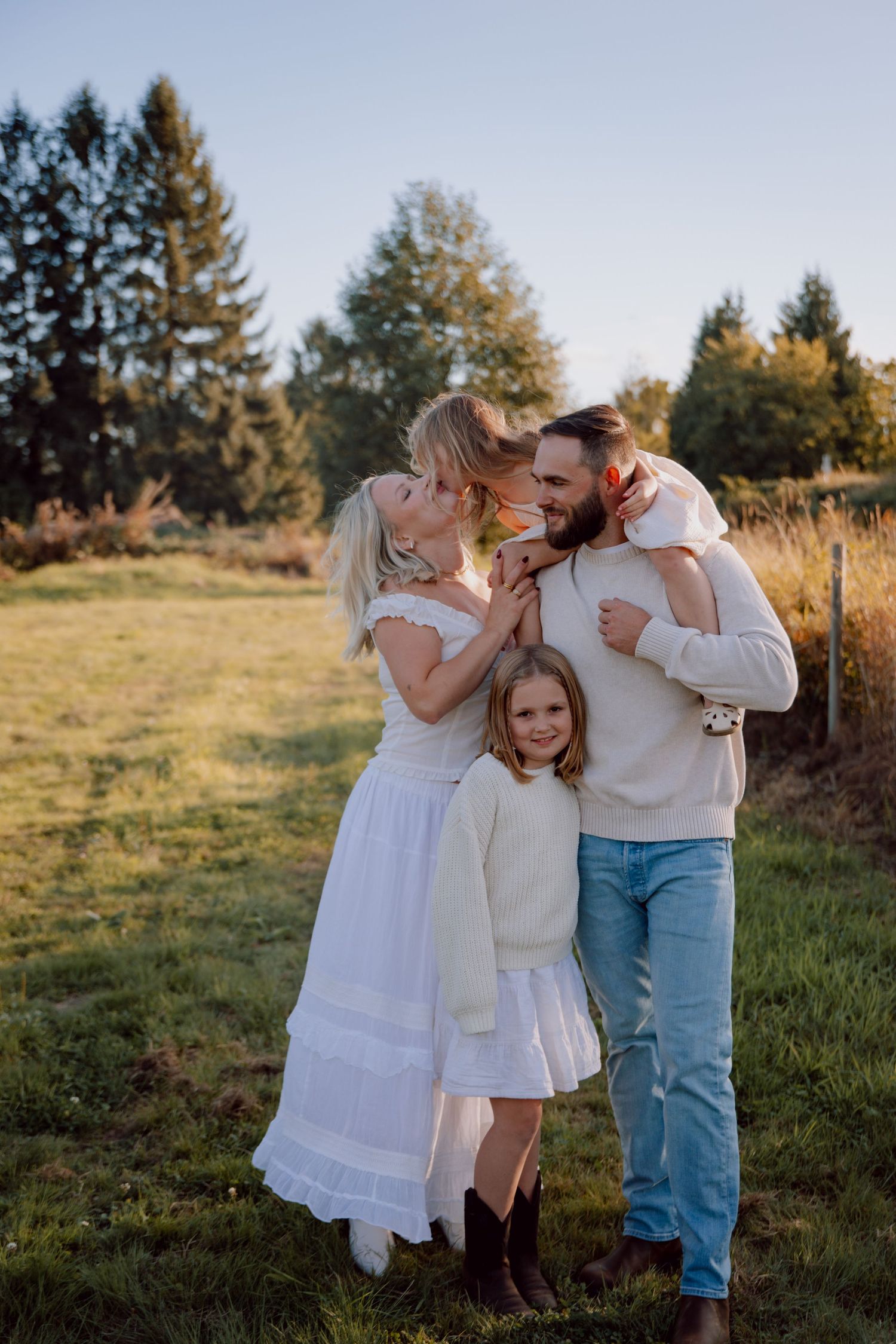 A family shares tender embraces and laughter in a sunlit meadow during golden hour photography session.