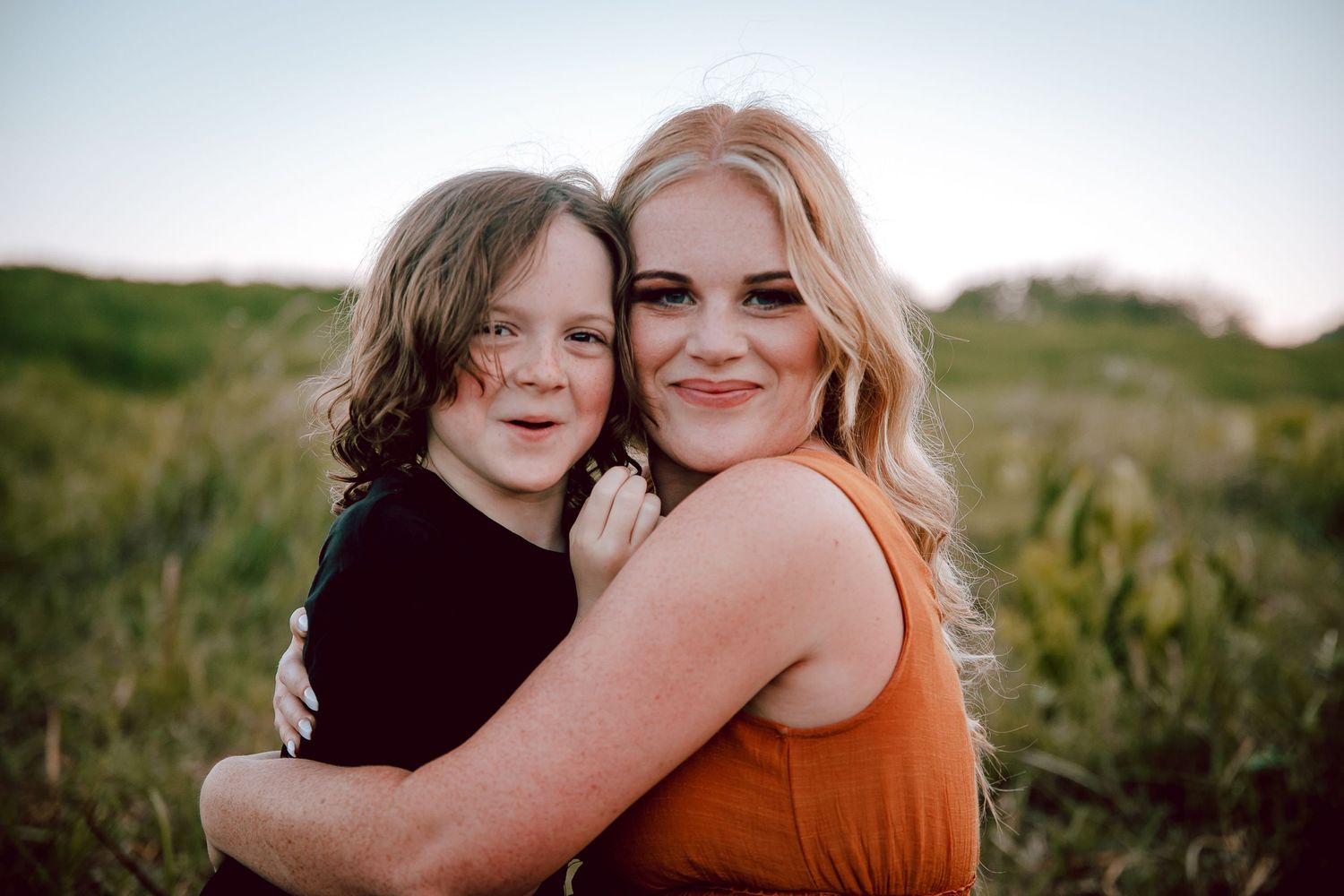 Mother and child share warm embrace outdoors in golden sunlight.