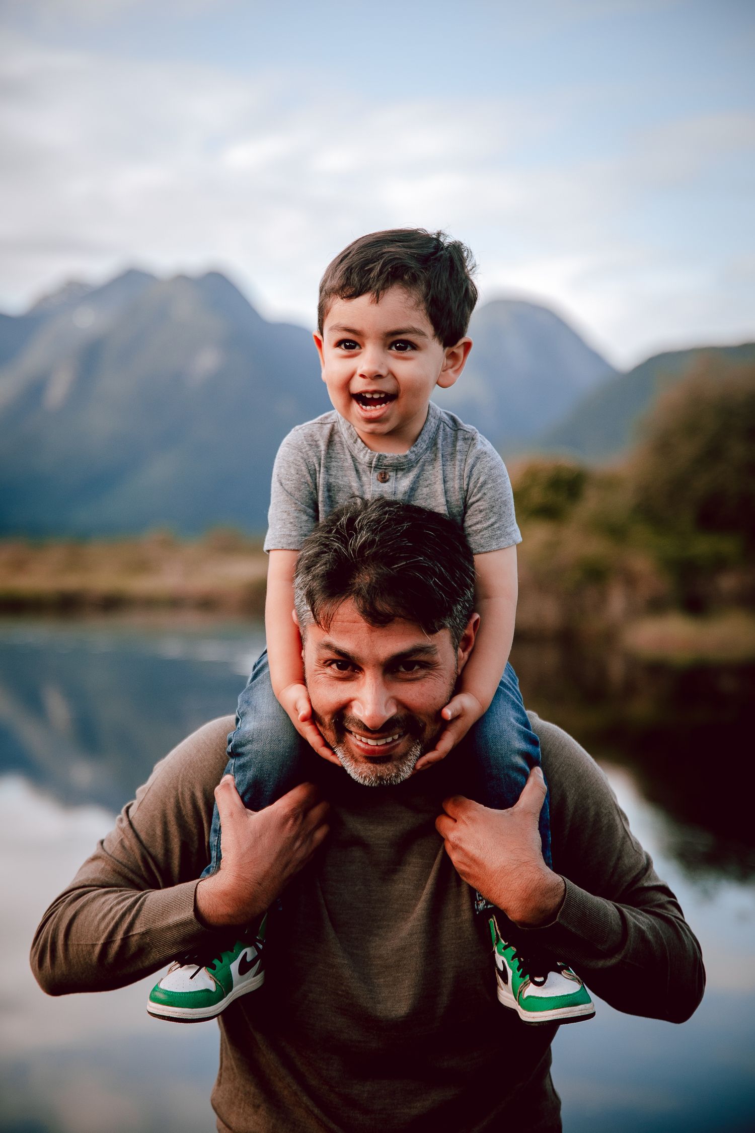 A joyful moment between parent and child enjoying the outdoors with mountains and a lake in the background.
