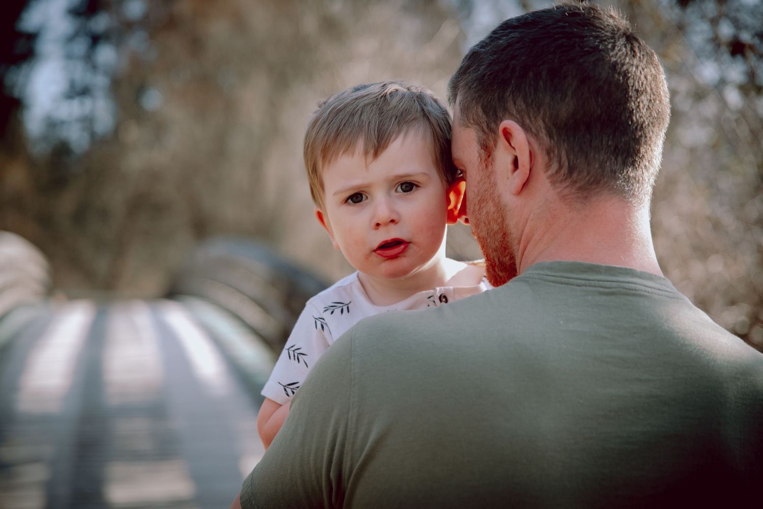A parent holding a young child close while standing outdoors.