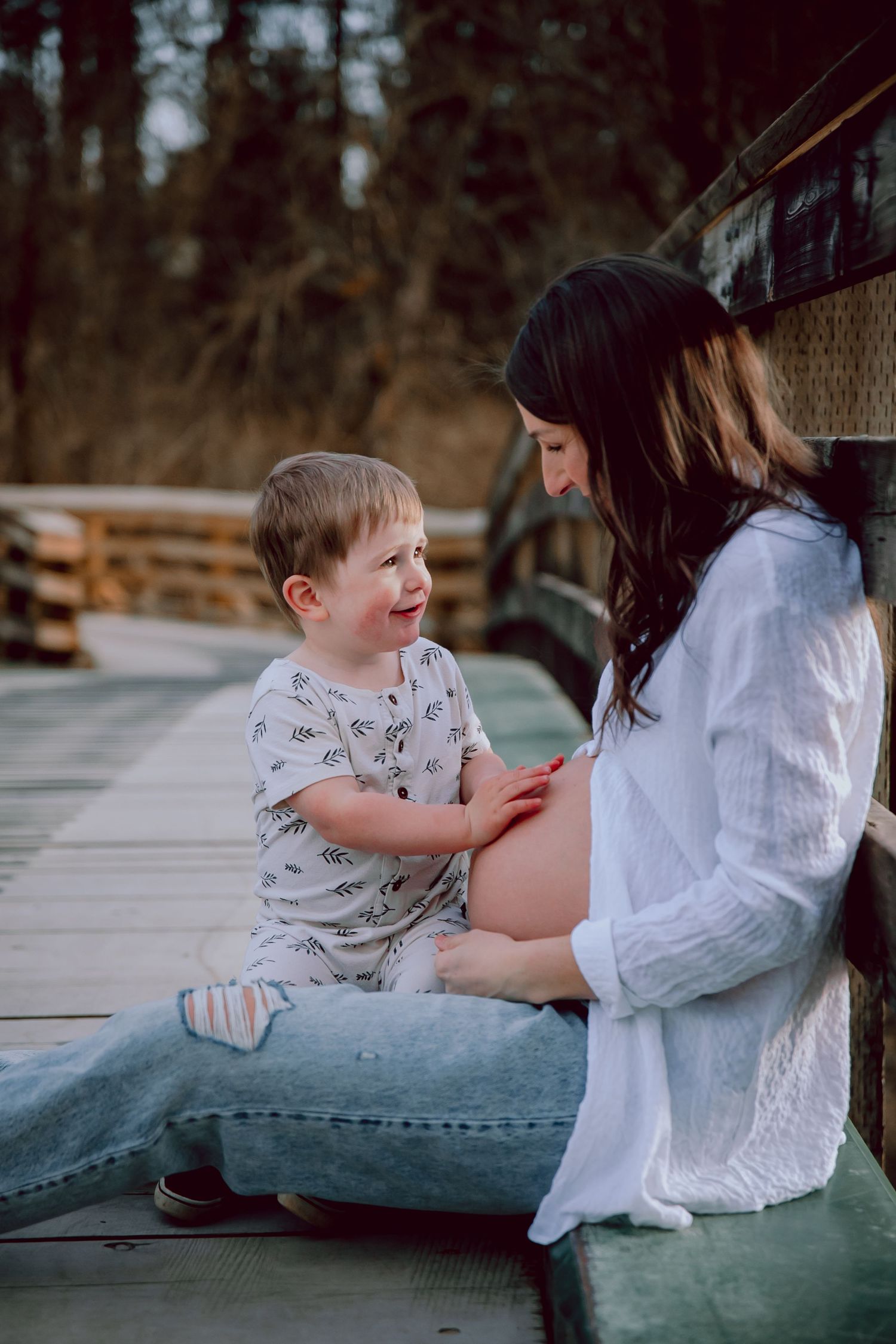 A touching maternity moment as toddler interacts with mother's pregnant belly on wooden boardwalk.