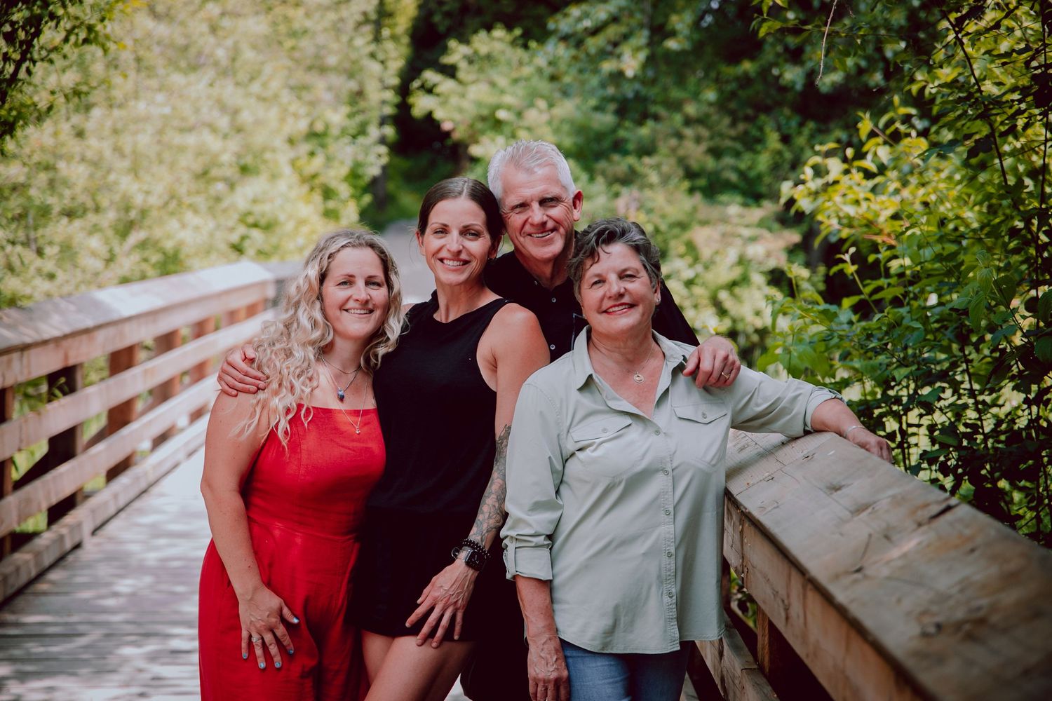 Group of four women pose together on a wooden bridge surrounded by lush greenery.