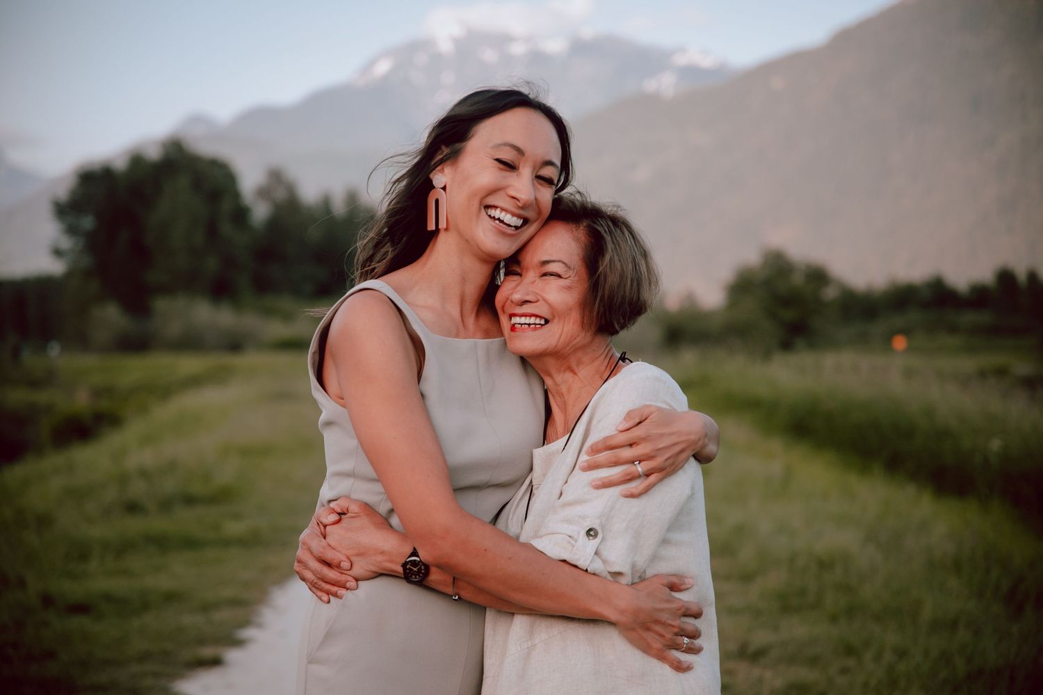 Two people embrace and laugh joyfully against a mountain backdrop at sunset.