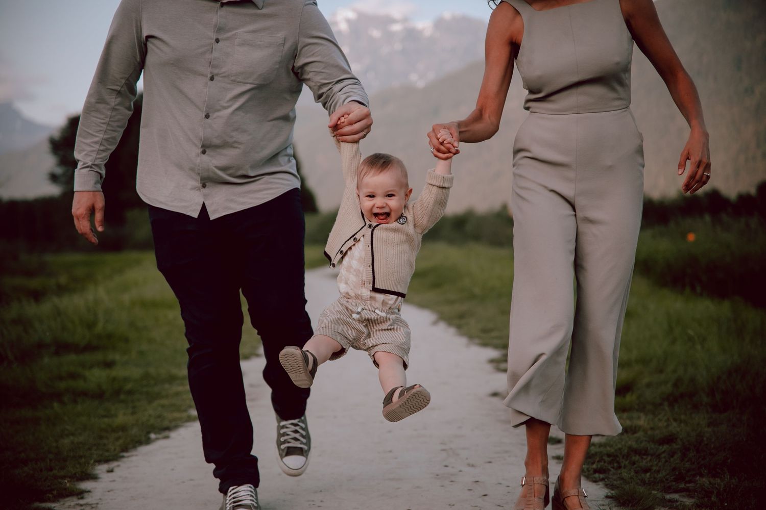 A young child swings between two adults while walking on a path with mountains in background.