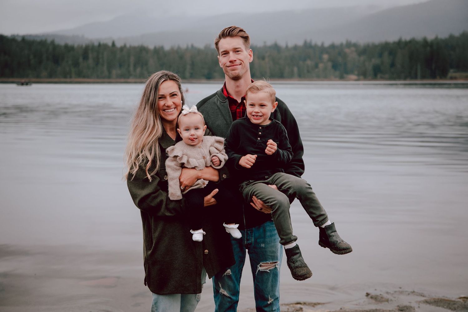 Family of four takes photo together by misty lake with mountains in background.