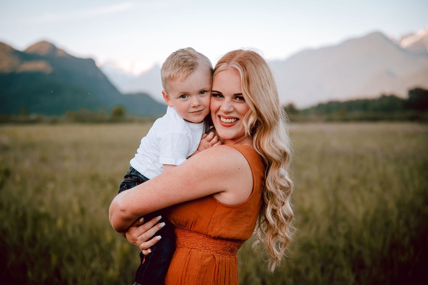 Mother in orange dress holds small child with mountain landscape in background.