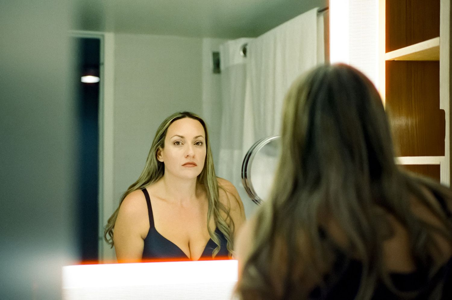 A woman looking at her reflection in a bathroom mirror during evening hours.