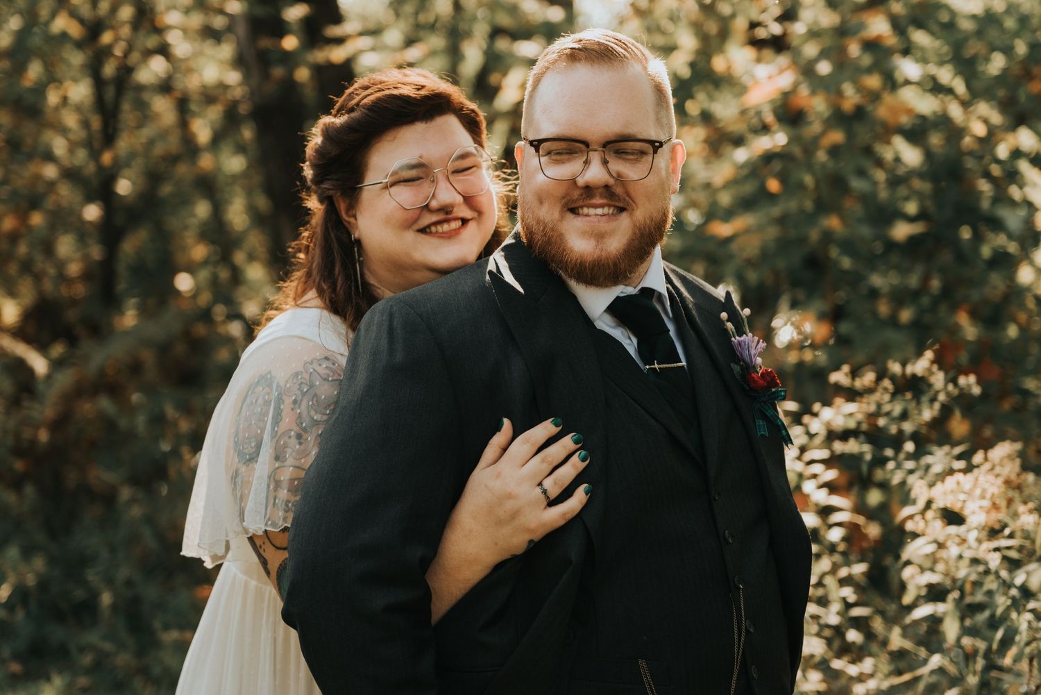 A loving couple poses outdoors on their wedding day with beautiful golden sunlight filtering through foliage behind them.
