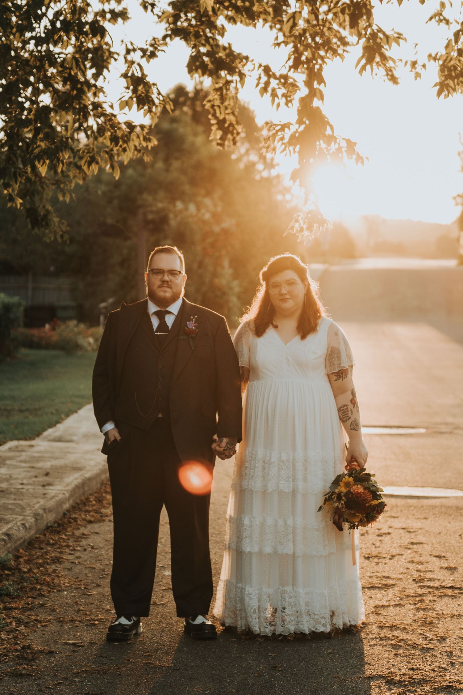 A beautiful sunset wedding photo of a couple holding hands on a path with golden light streaming through autumn leaves.
