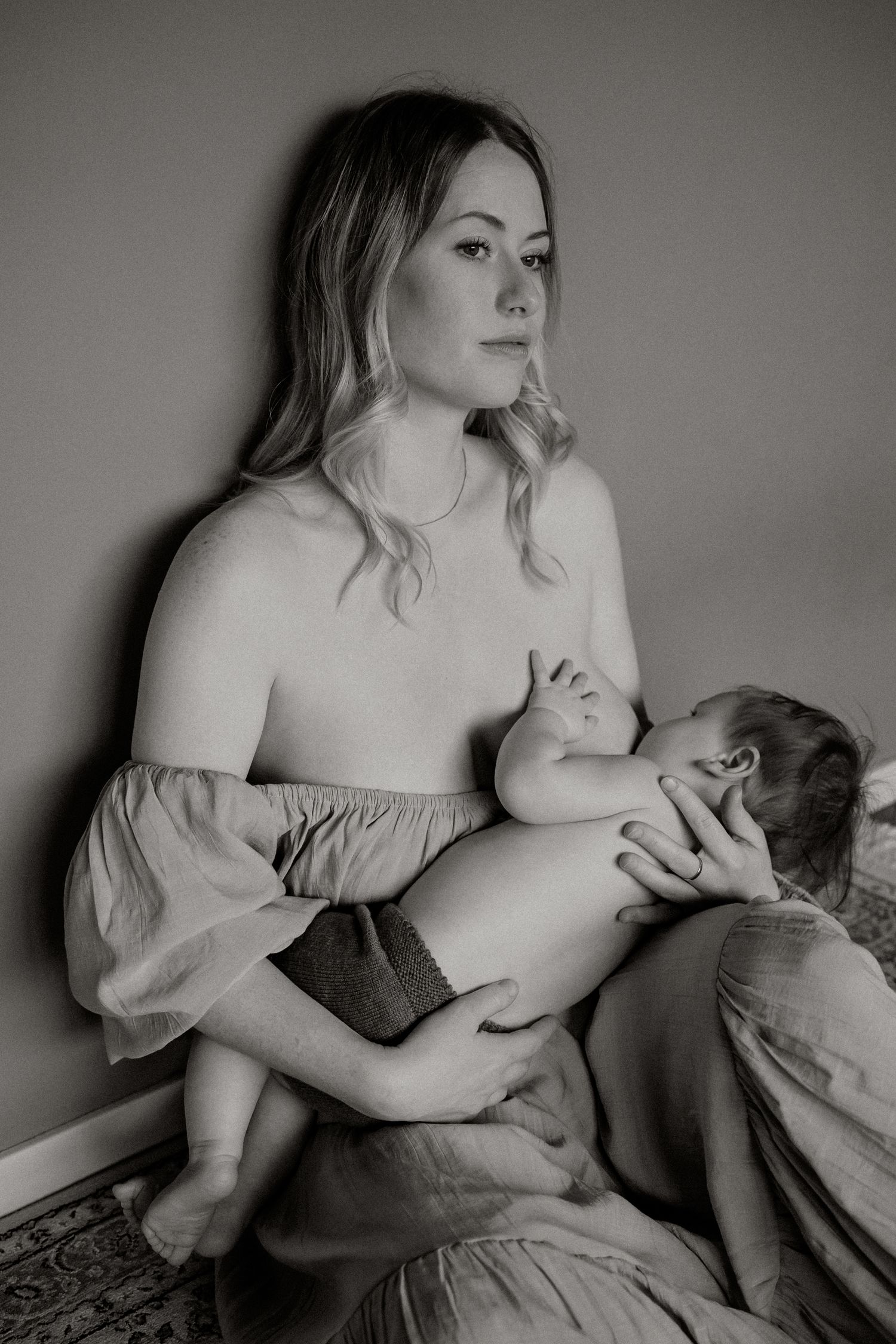 Een zwart-wit intiem portret van een moeder die haar baby voedt in zacht natuurlijk licht.