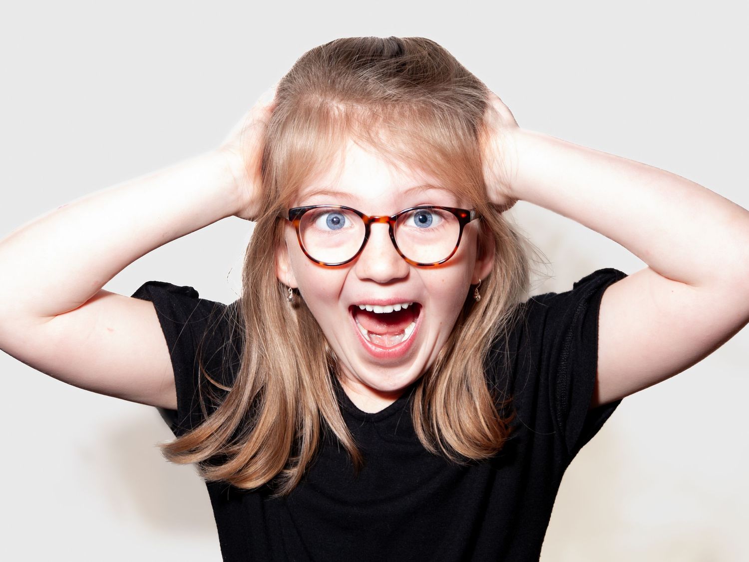 Laughter and personality shine in this playful portrait of a girl reacting with astonishment, hands raised and mouth open wide.