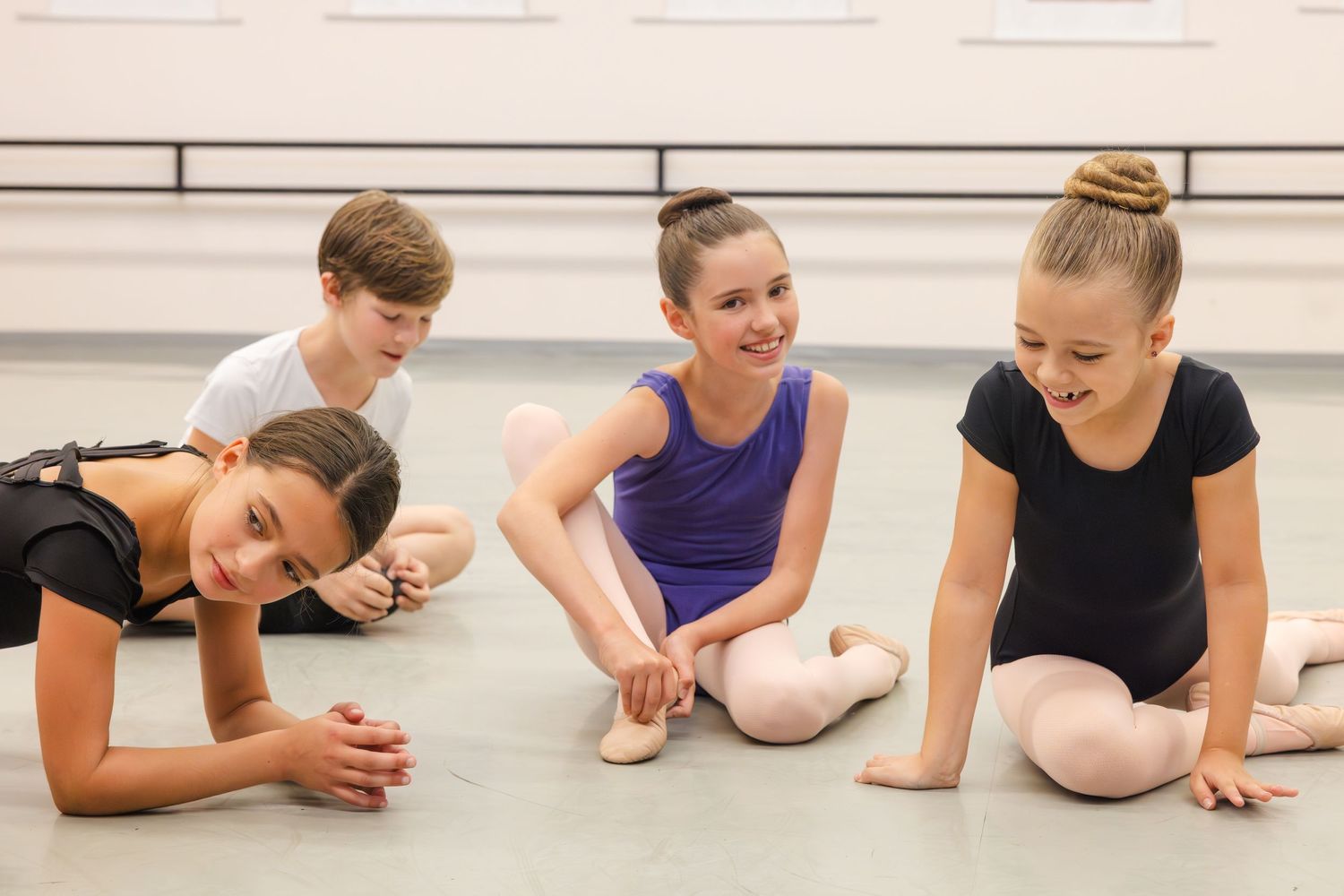 Young dancers in leotards taking a break and relaxing on the dance studio floor during ballet class.
