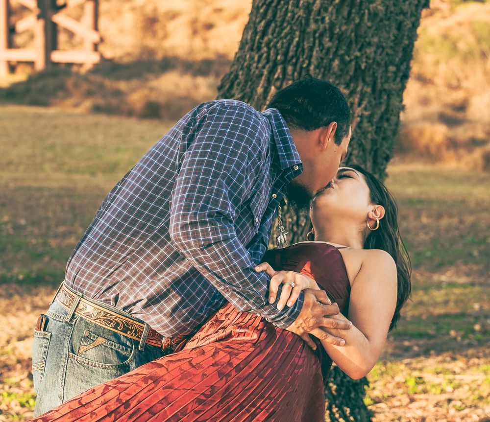 A romantic couple in western attire share an intimate moment while leaning against a tree during golden hour.