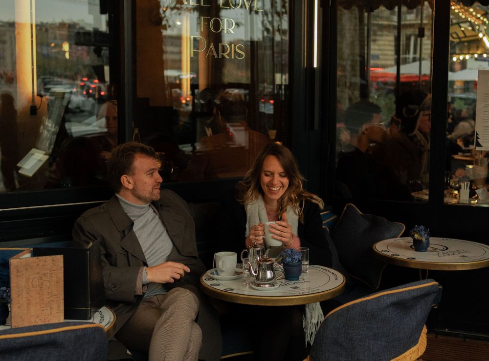 A couple enjoys coffee and conversation at an outdoor Parisian cafe table on a cozy autumn evening.