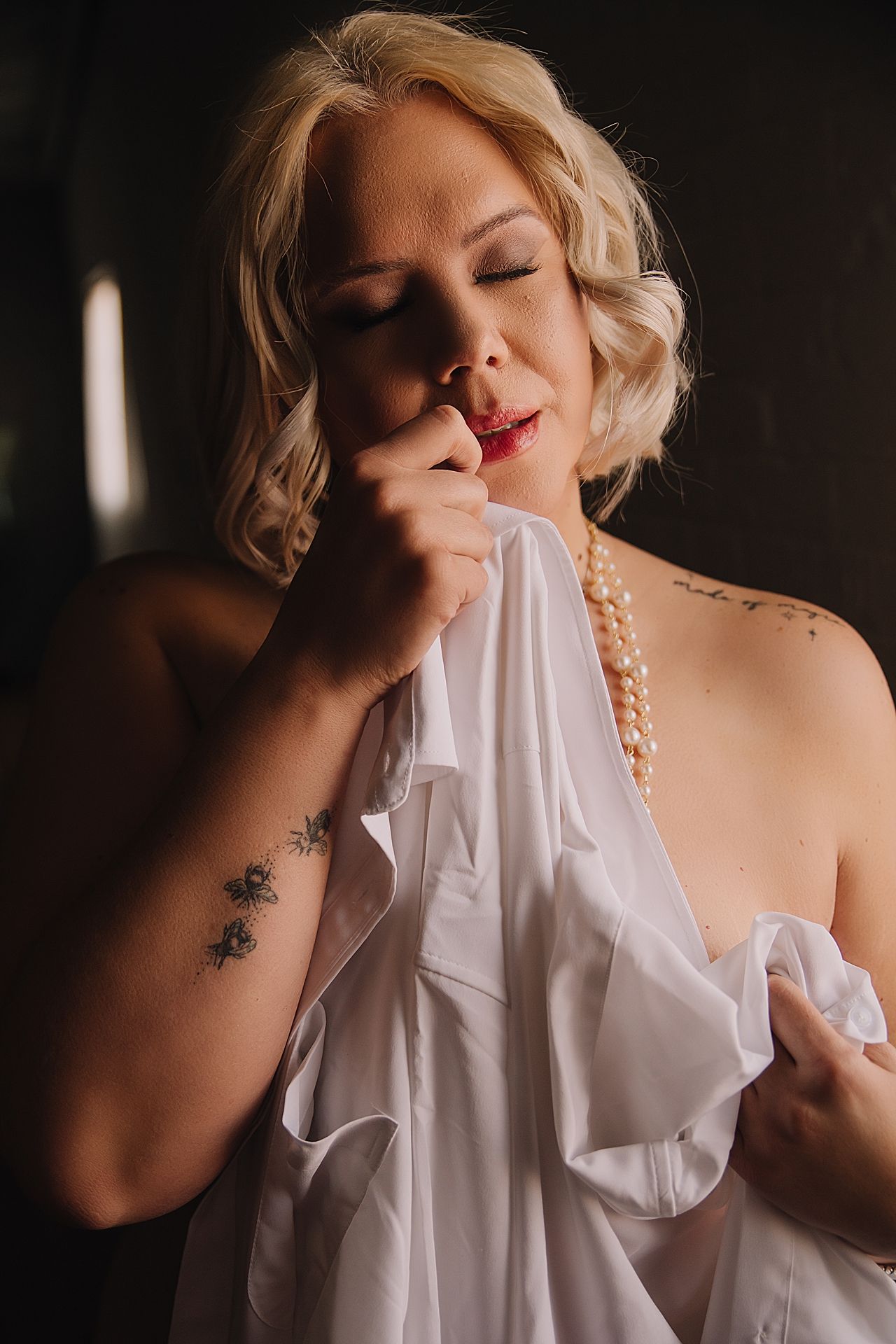 Dark and moody Utah Boudoir photo with woman in pearls and men's white button up shirt