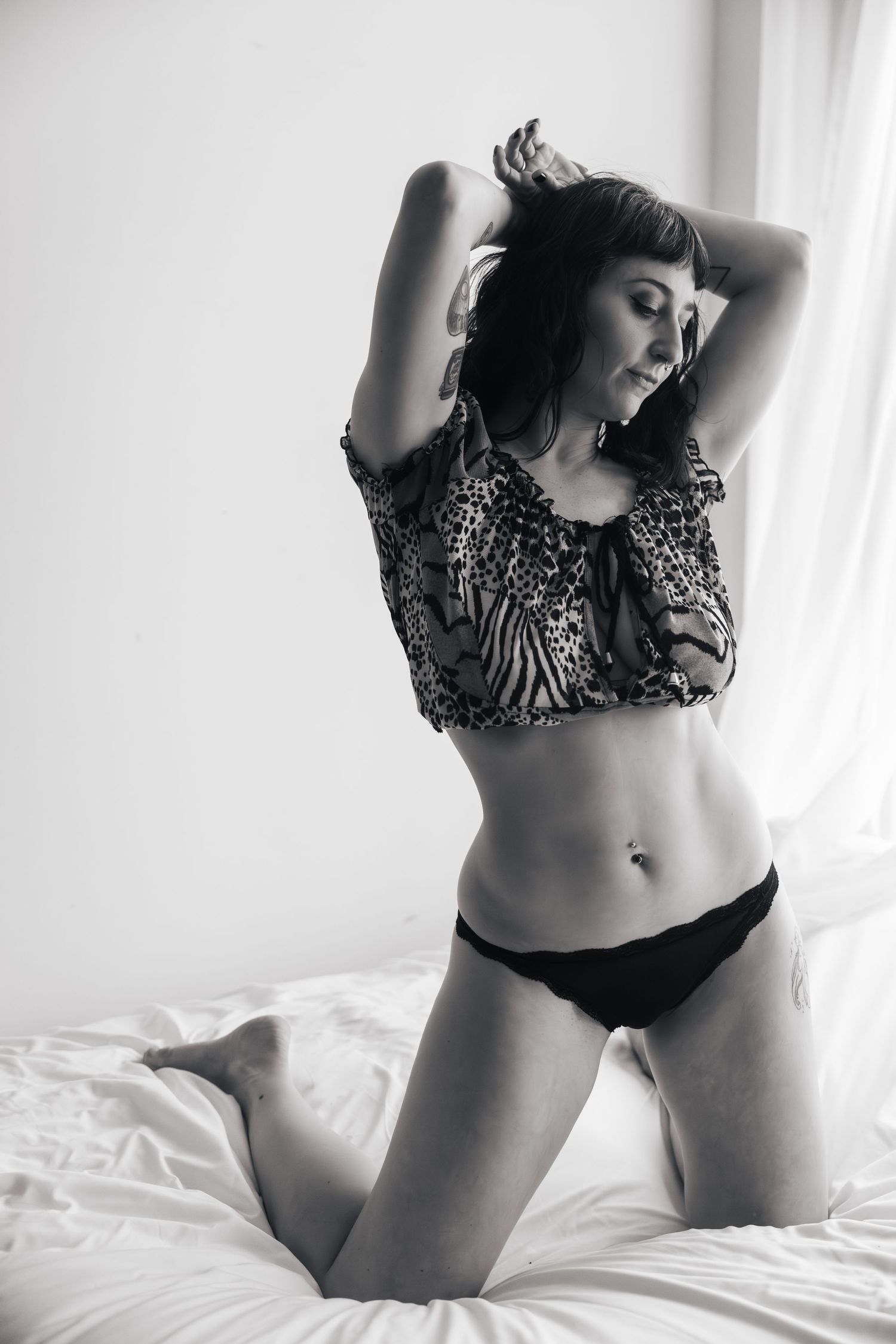 Black and white boudoir photo on white bedding showing a person in animal print top and dark bottoms.