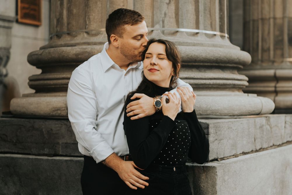 A couple shares an intimate embrace in front of classic stone columns during an engagement photo session.