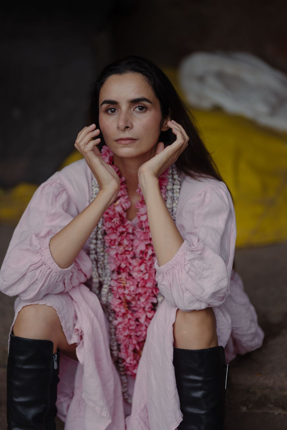 Person wearing pink dress and black boots poses against dark background.