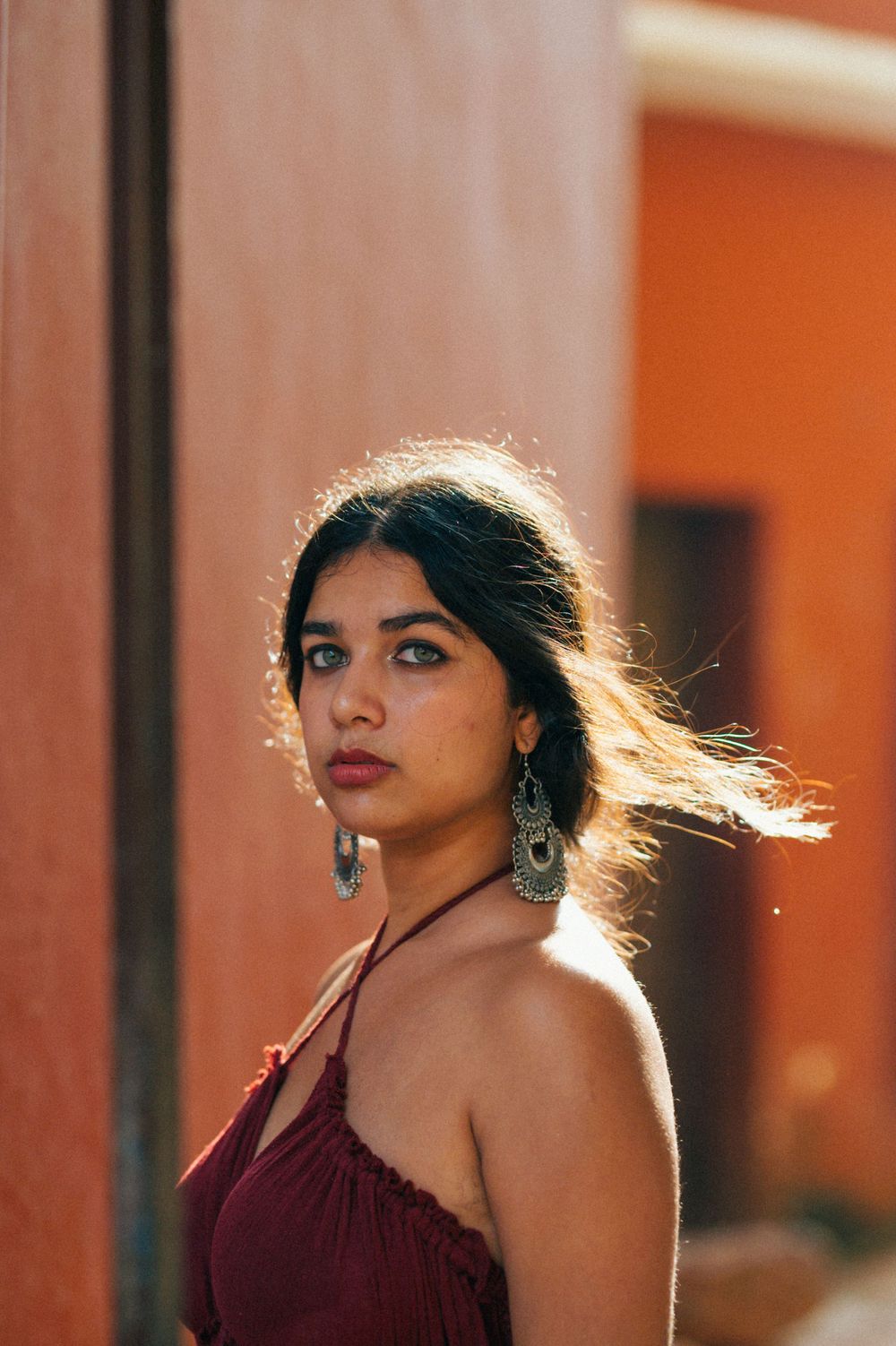 Backlit portrait in burgundy dress with dramatic rim lighting against orange wall.