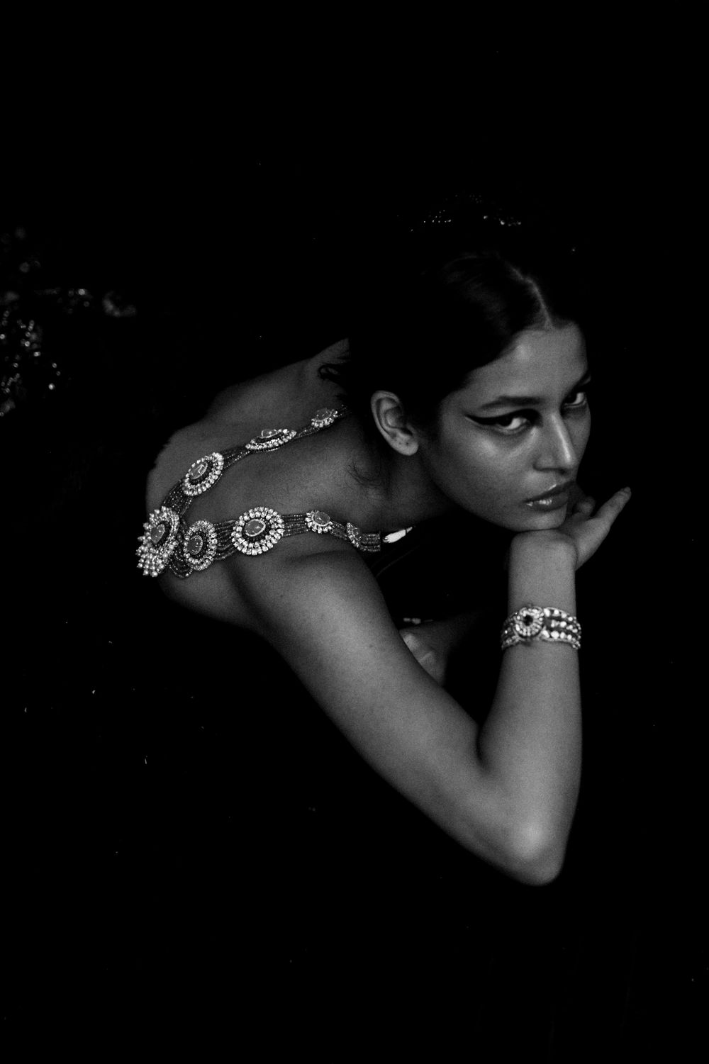 Black and white portrait showing decorative jewelry accessories against dark background.