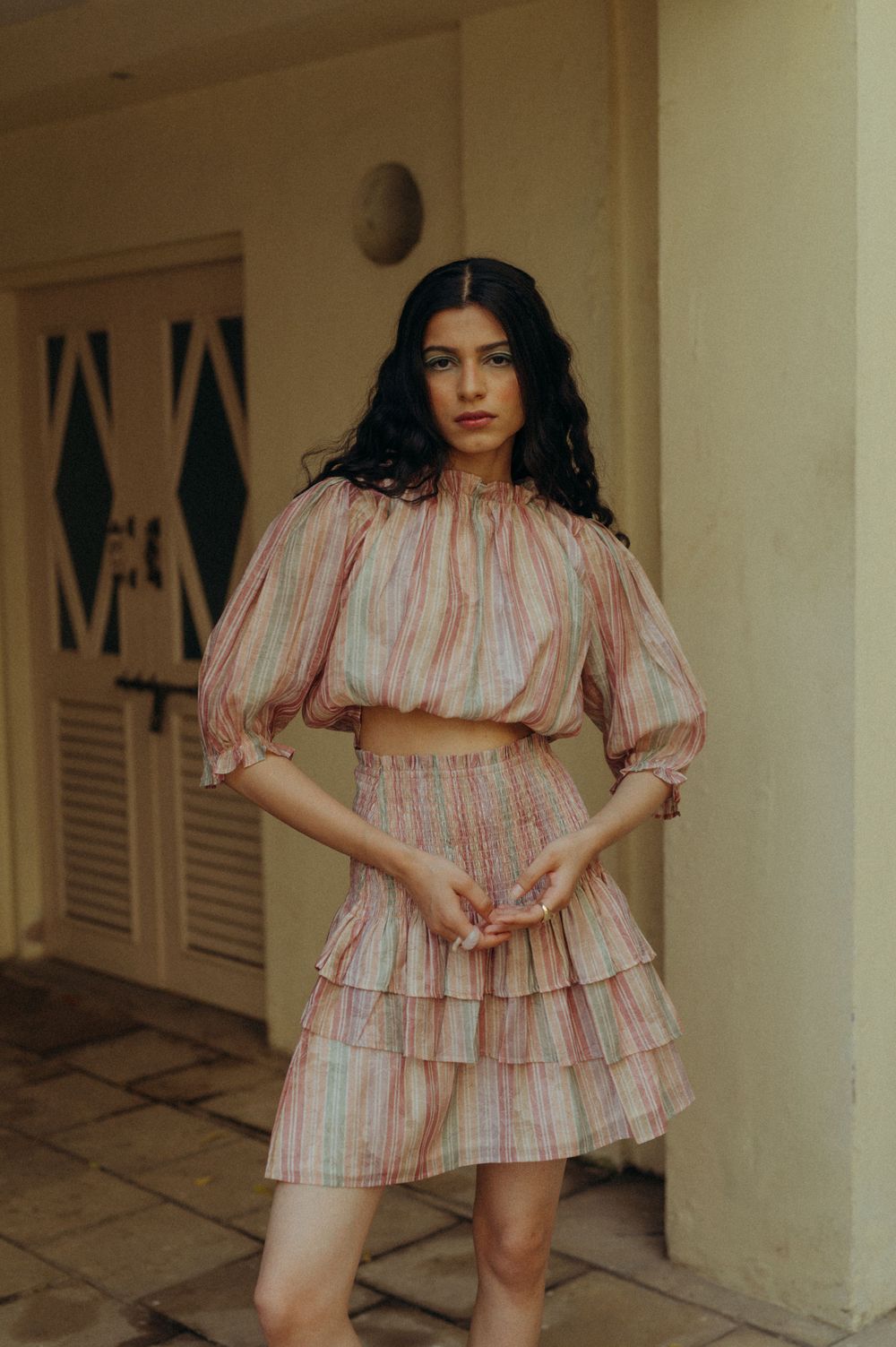 A fashionable striped pink dress with ruffled layers photographed against a beige wall.