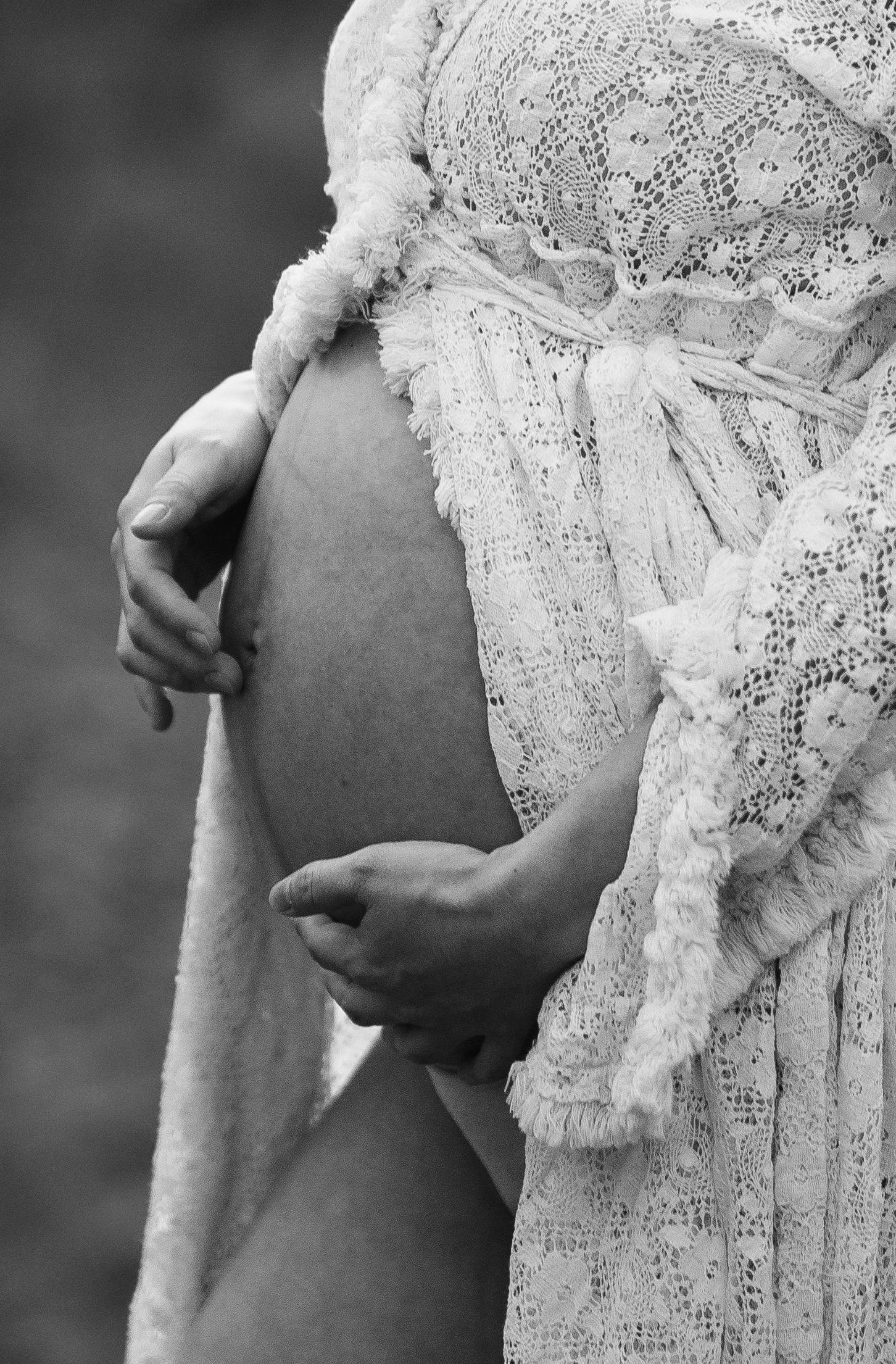 A black and white photo shows a pregnant belly being cradled while wearing delicate lace fabric.