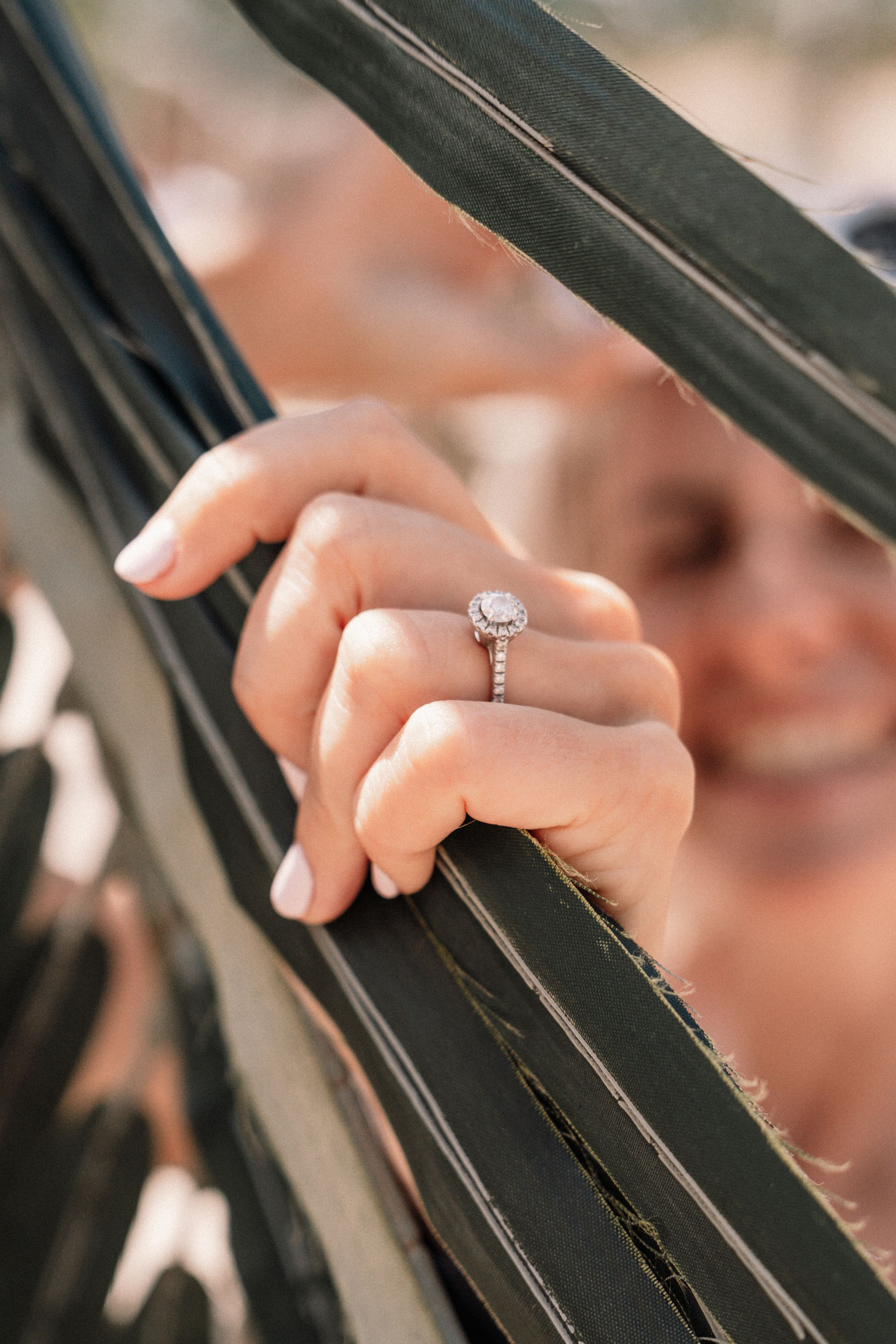 Close-up of sparkling diamond engagement ring on woman's hand resting against black railing.
