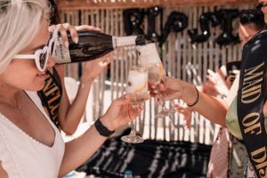 Women toasting and drinking champagne at an outdoor party under wooden pergola.