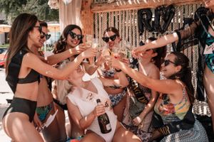 Group raising champagne glasses in celebration at a tropical beach party.