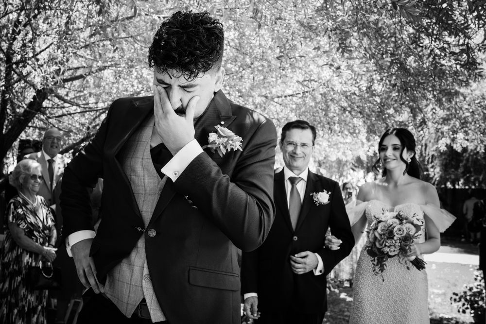 Black and white candid wedding photograph captures an emotional moment during outdoor ceremony in a park setting.