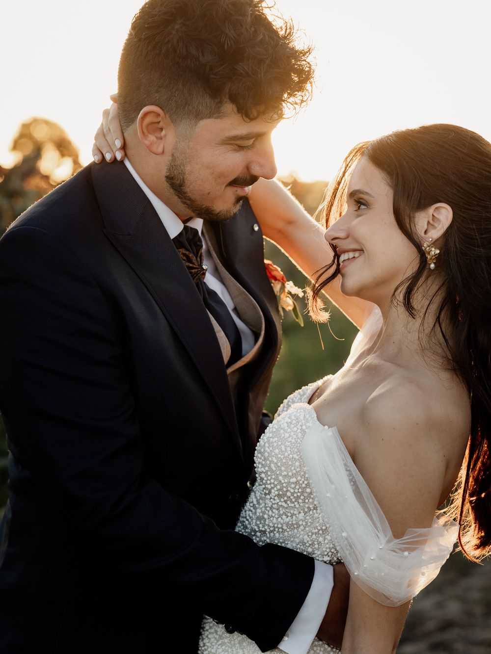 A romantic wedding couple sharing an intimate moment at sunset in formal attire.