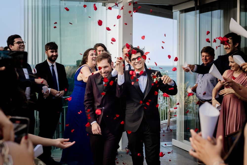 Wedding guests throw red rose petals as newlyweds exit their ceremony celebration.
