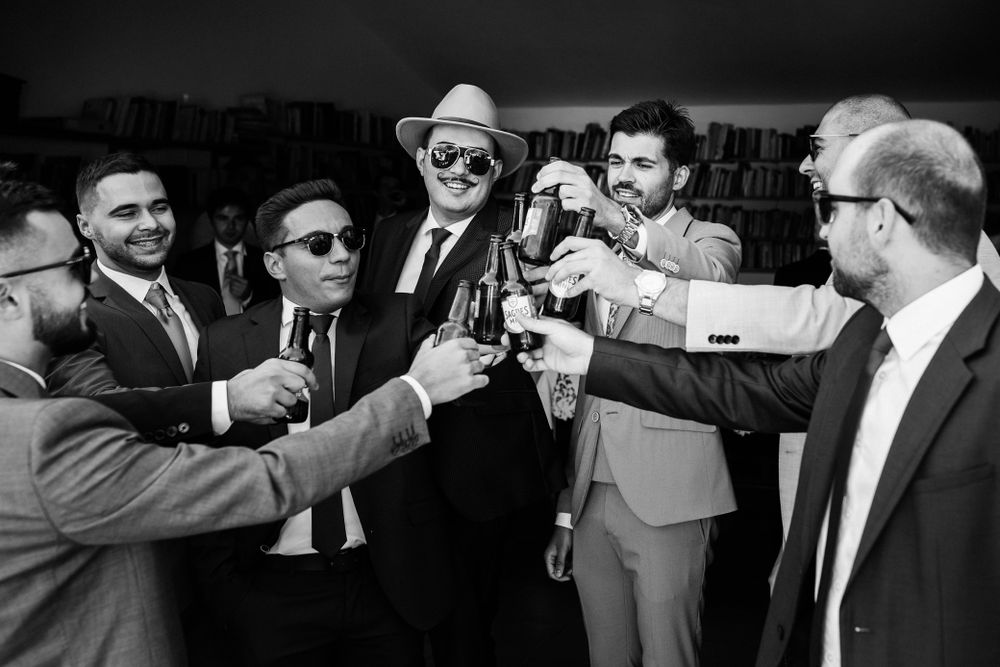 A group of men in suits and sunglasses raise their glasses in a celebratory toast at a formal event.