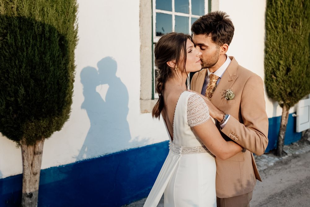A romantic moment at sunset with shadow silhouettes cast on a white wall beside tall cypress trees.