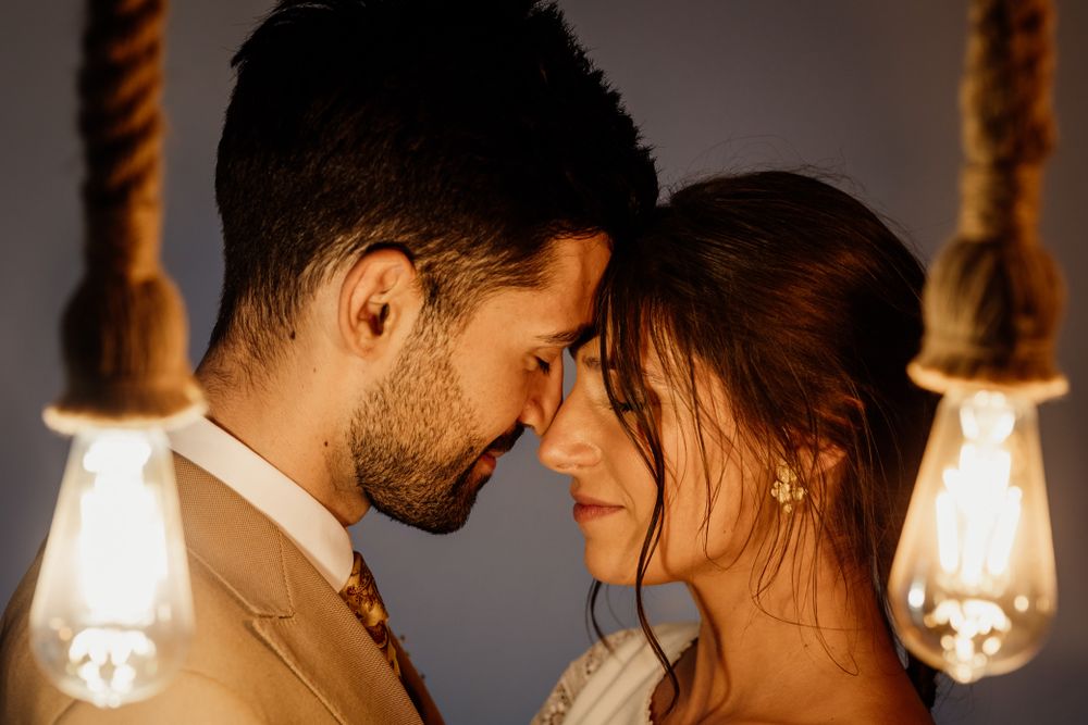 Intimate romantic moment between couple illuminated by warm glowing Edison bulbs on rope in dark room.
