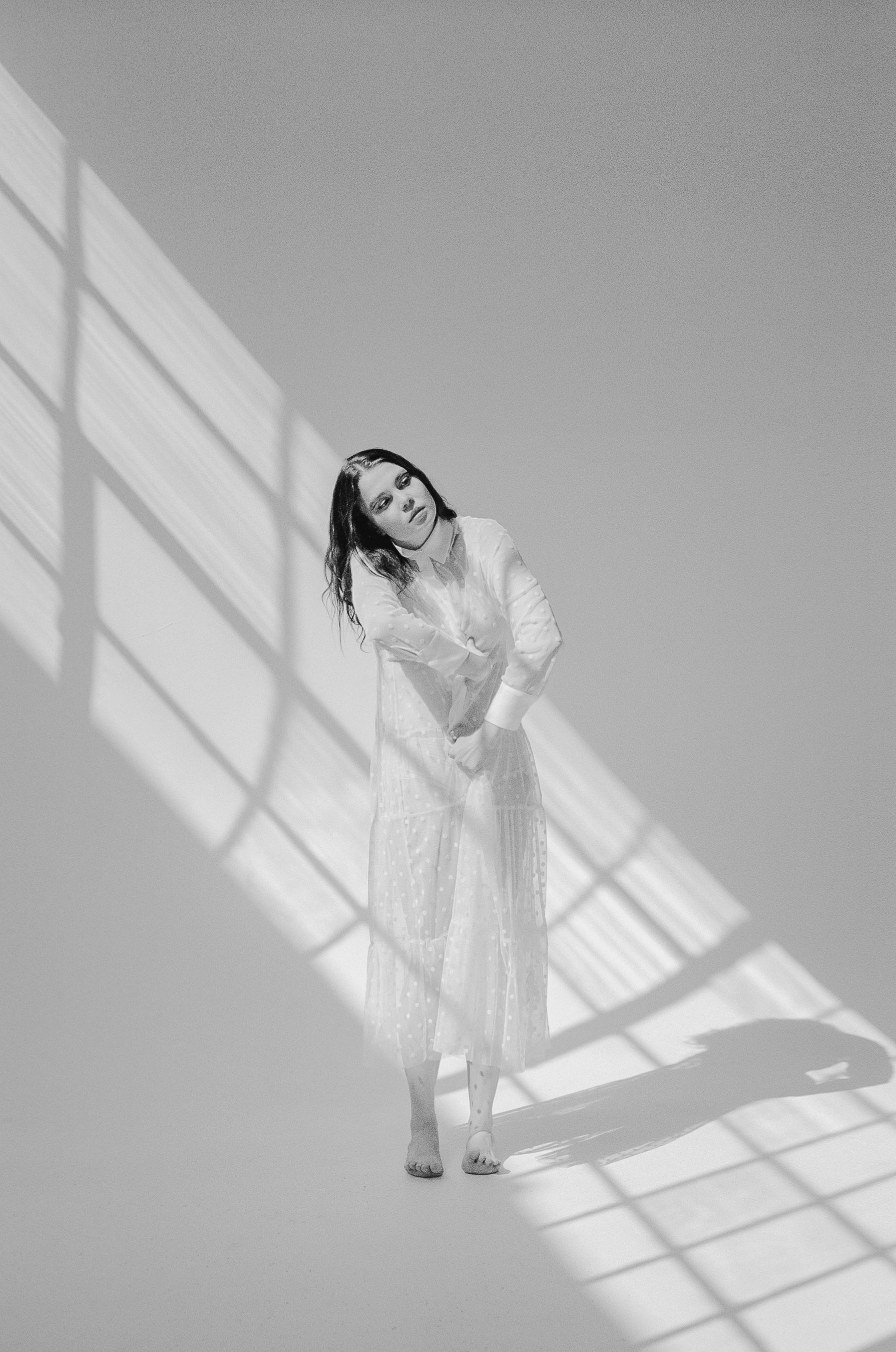 Minimalist black and white portrait of person in white dress posing in geometric window light.