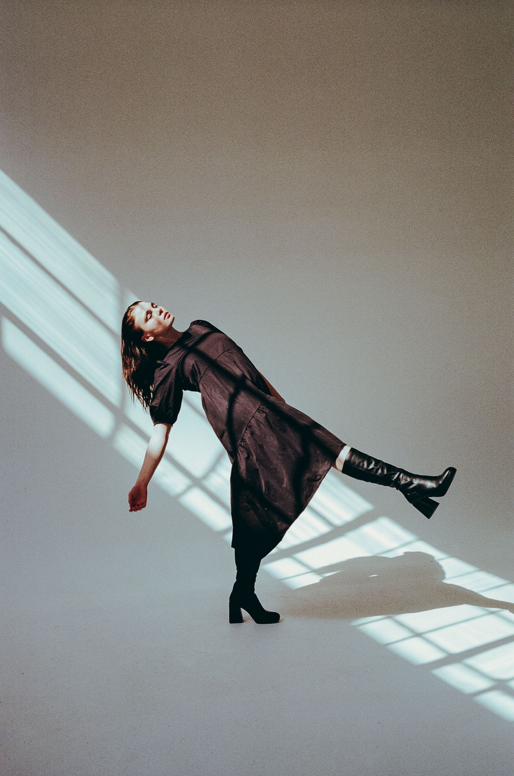 Artistic portrait of a dancer in a dark dress leaning back in dramatic window light.