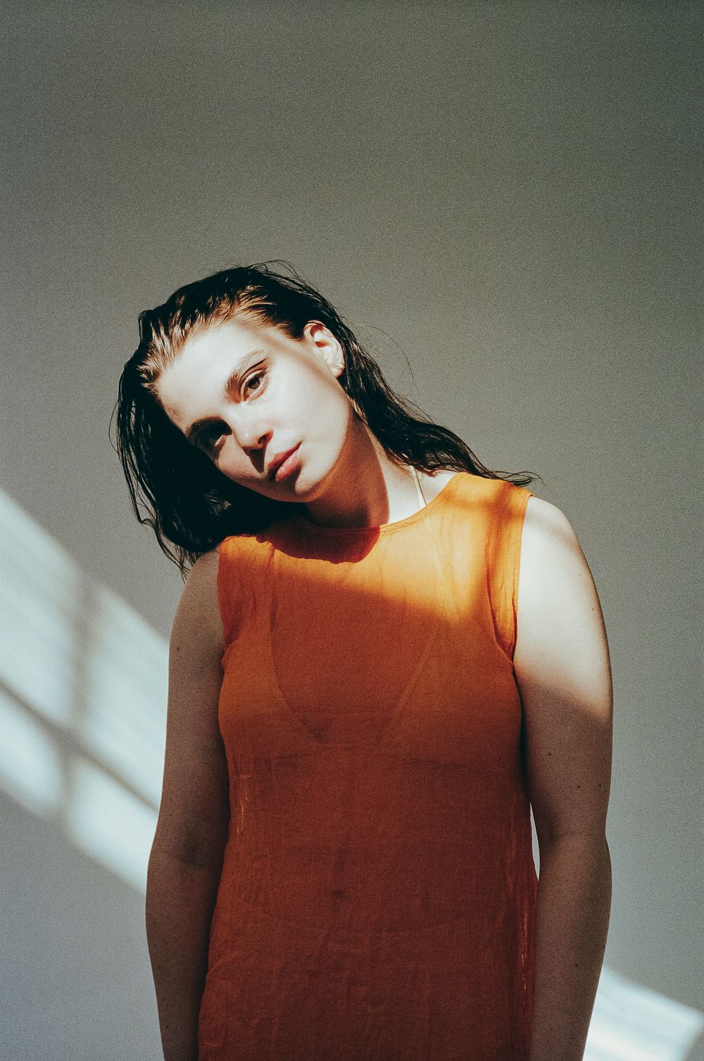 Portrait in an orange sleeveless top with natural window light creating diagonal shadows.