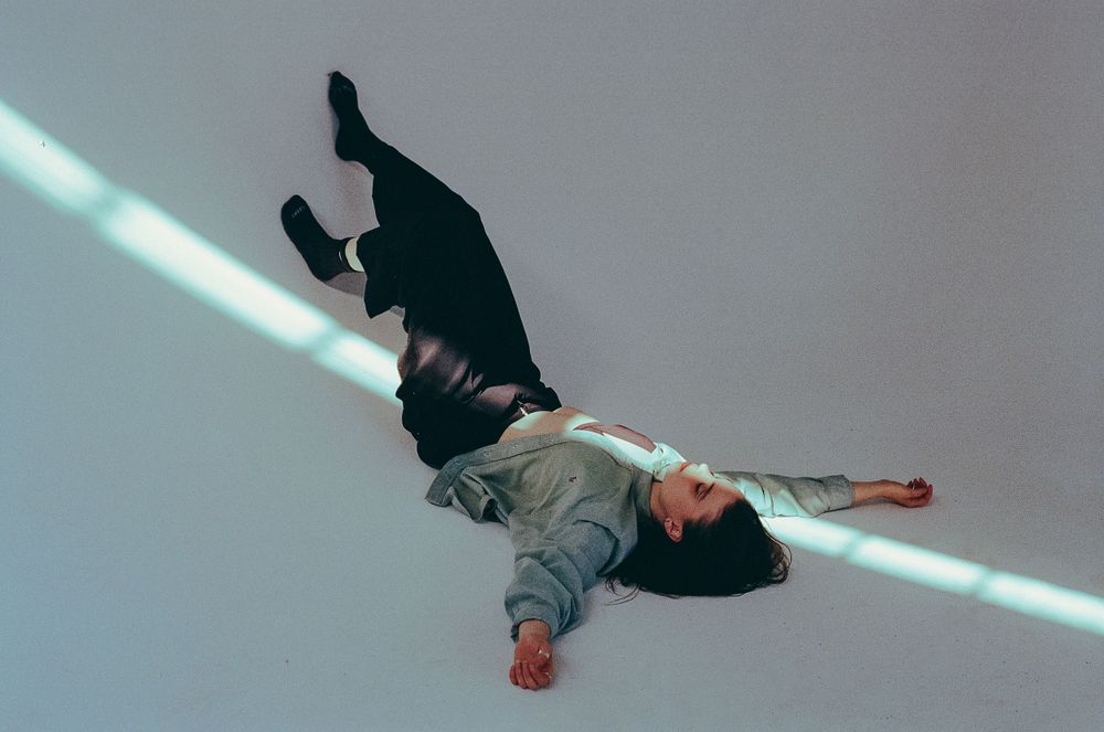 Figure in dark clothing lying horizontally with a beam of light across the composition.