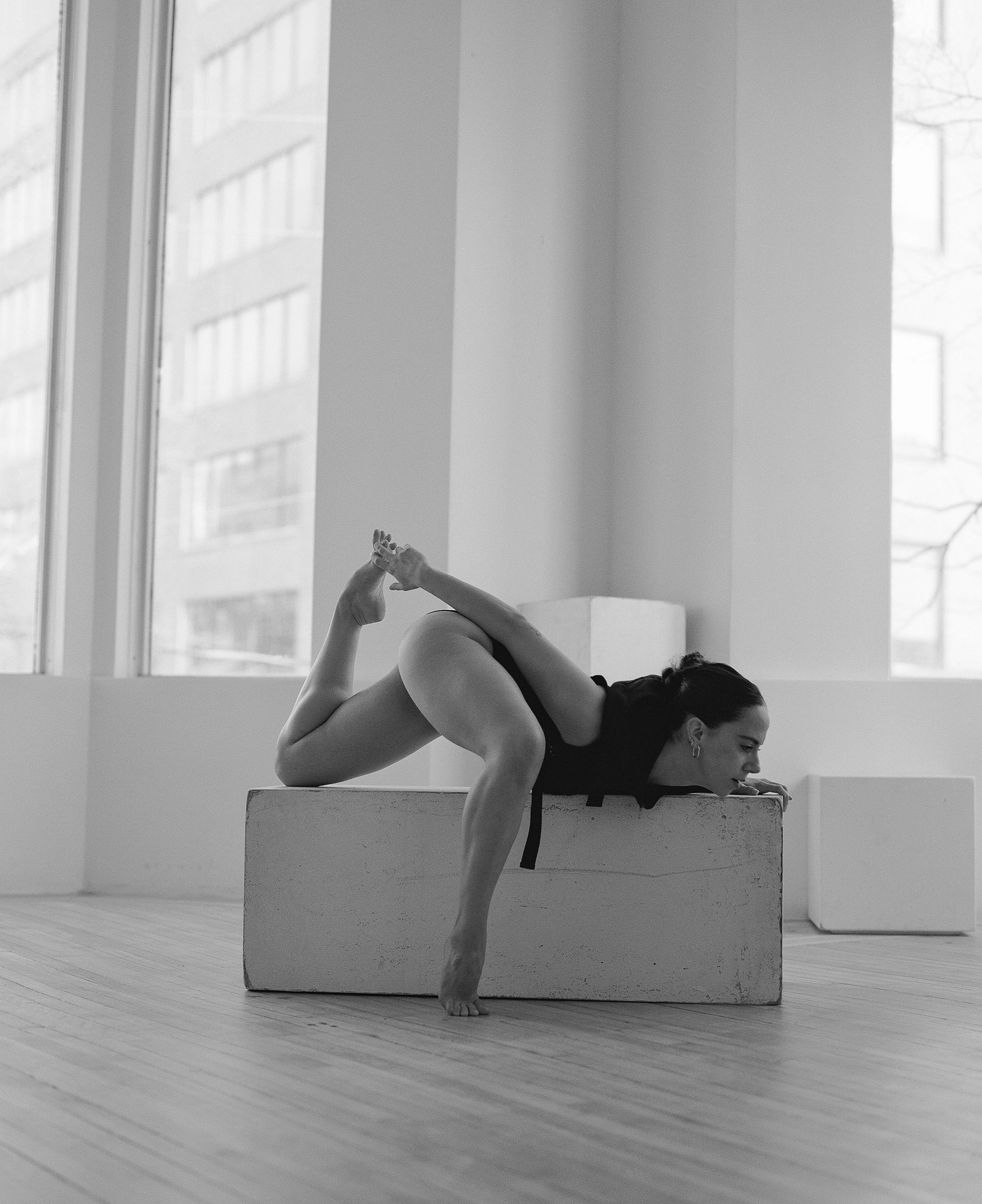 Contemporary dancer performs abstract pose on white cube in minimalist studio setting.