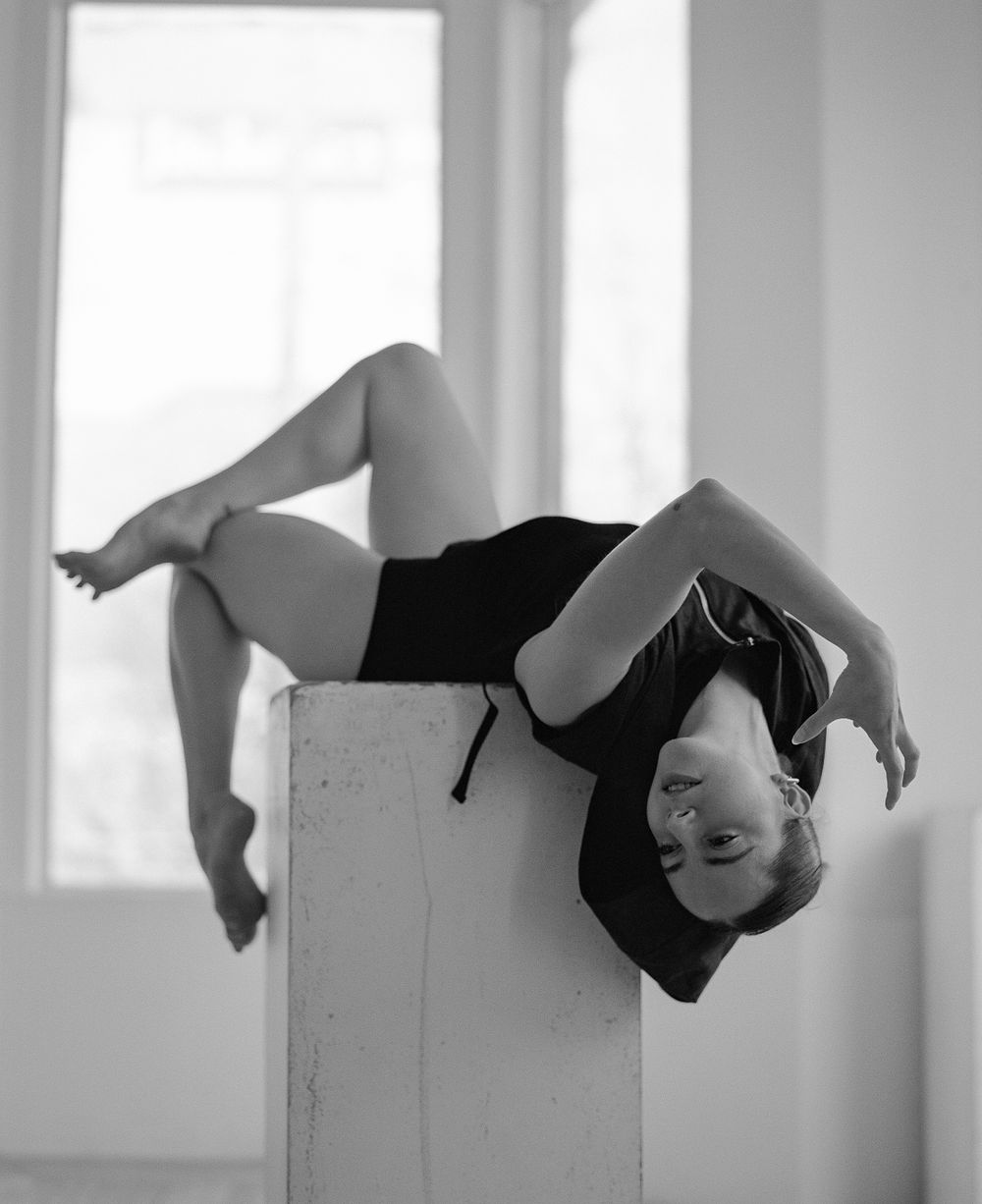 Dramatic black and white dance photo showing inverted pose on white pedestal.
