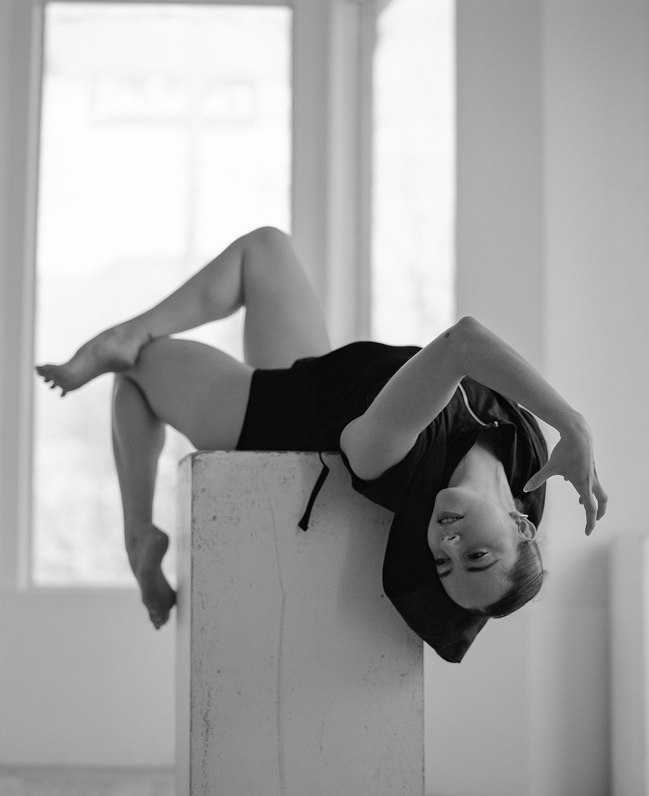 Dramatic black and white dance photo showing inverted pose on white pedestal.