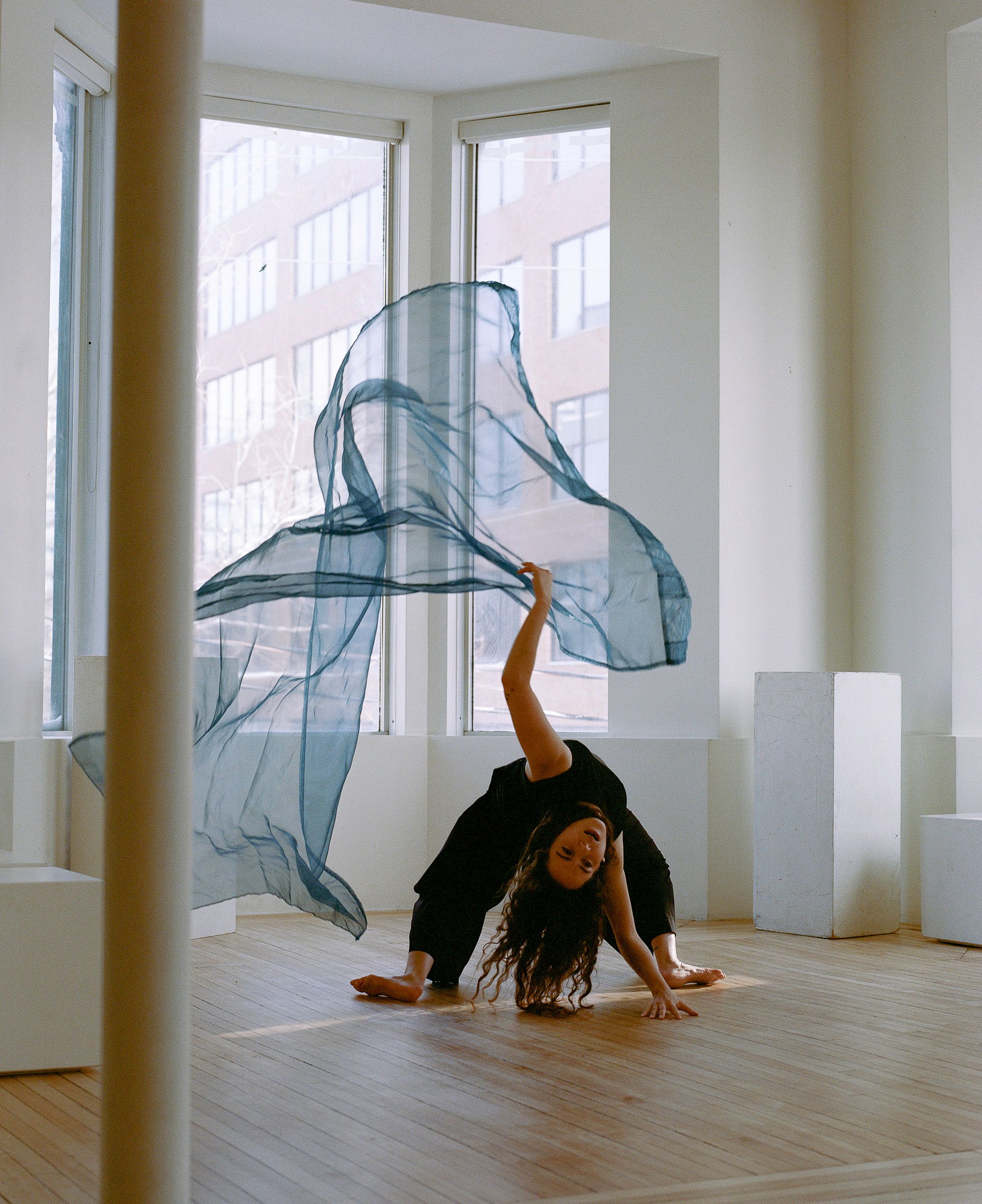 Modern dancer performing with flowing blue fabric in sunlit studio space.