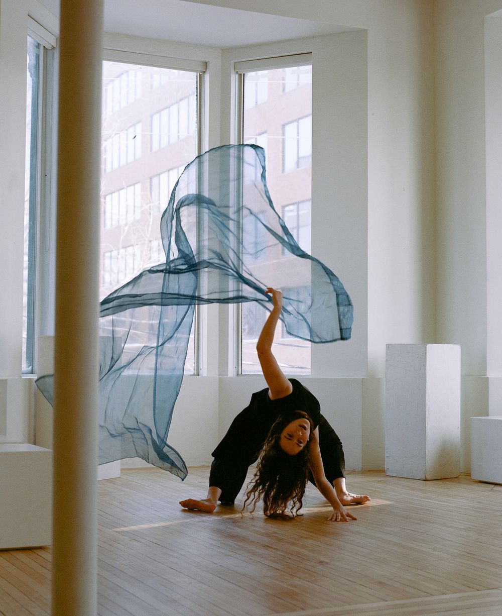 Modern dancer performing with flowing blue fabric in sunlit studio space.