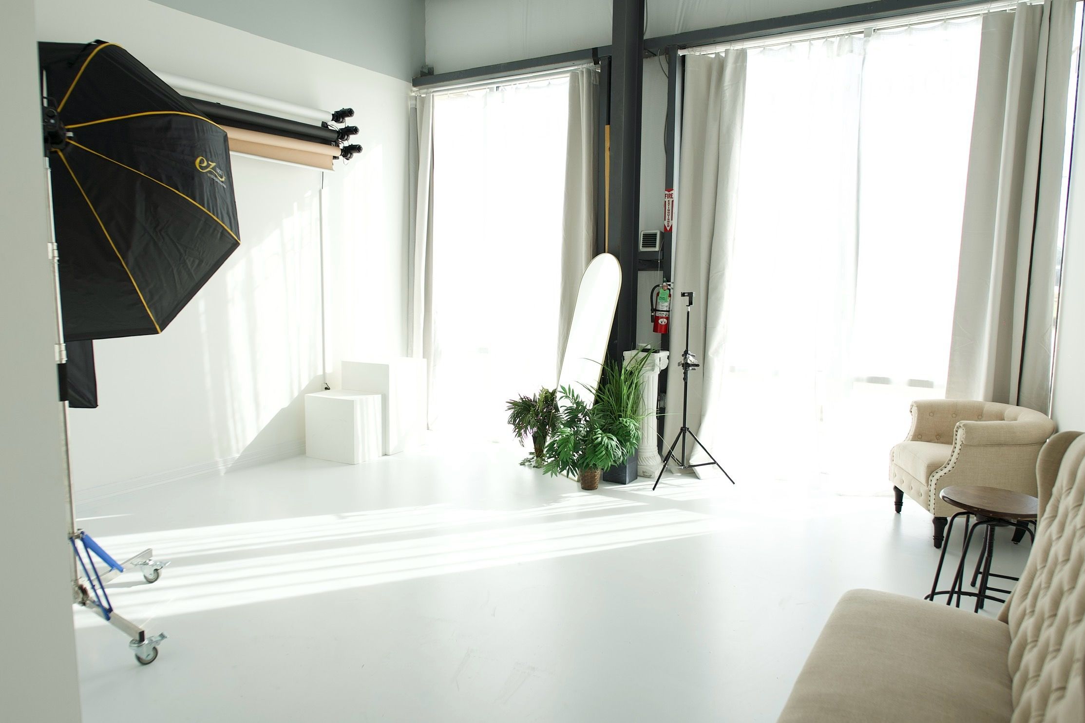 A photography studio setup with lighting equipment and white backdrop near large windows.